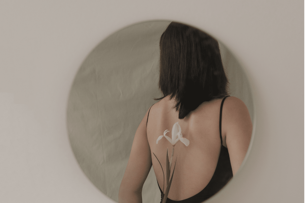 Someone holding a flower behind their back and facing away. The shot is framed in an off-white circle