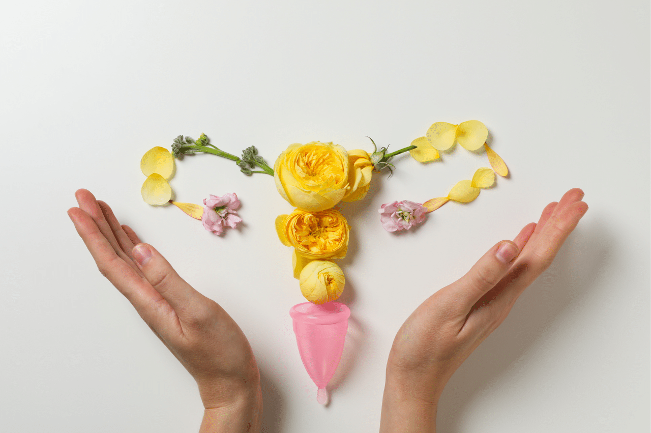 Hands surrounding uterus made out of flowers and a menstrual cup