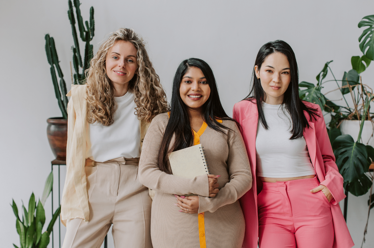 Photo of 3 young women in business casual attire standing side by side smiling