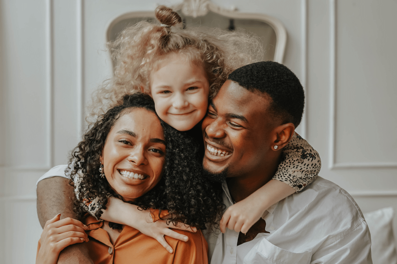 Photo of a young girl standing behind her parents with arms around them