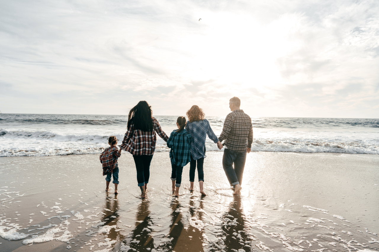 Photo of a family of 5 looking out at the ocean on the sand.