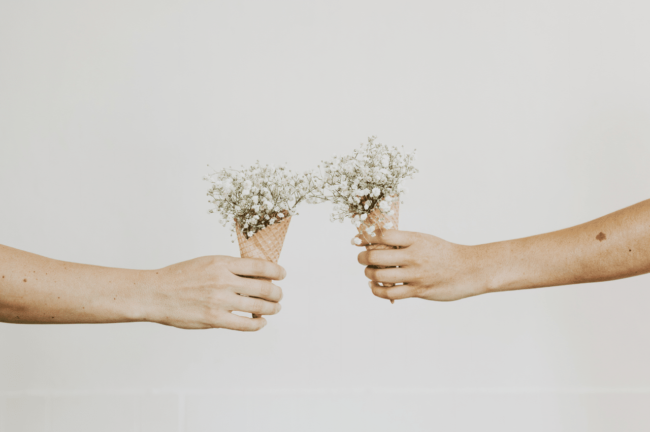 Photo of 2 arms holding a waffle cone full of white wildflowers against a cream background