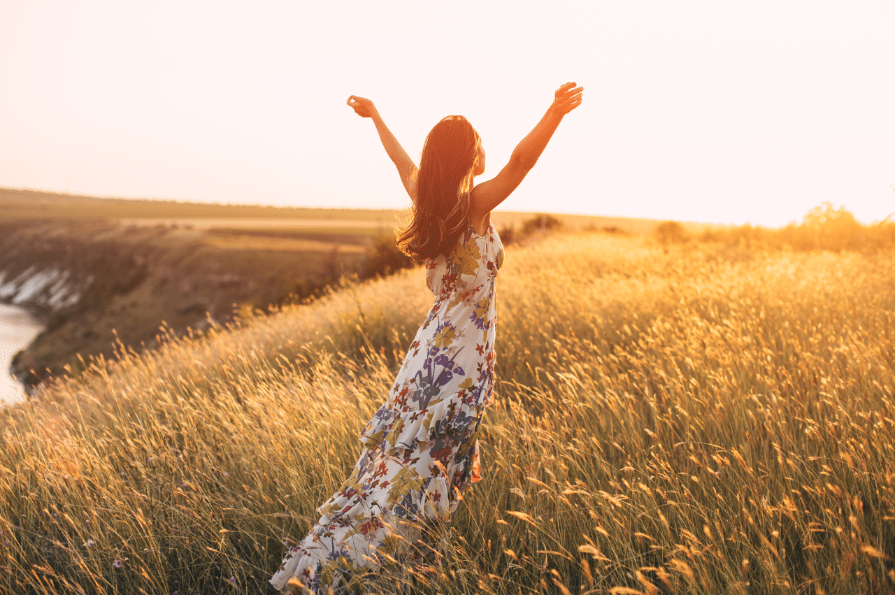 Photo of a woman in a field wearing a flowy dress with her arms to the sky