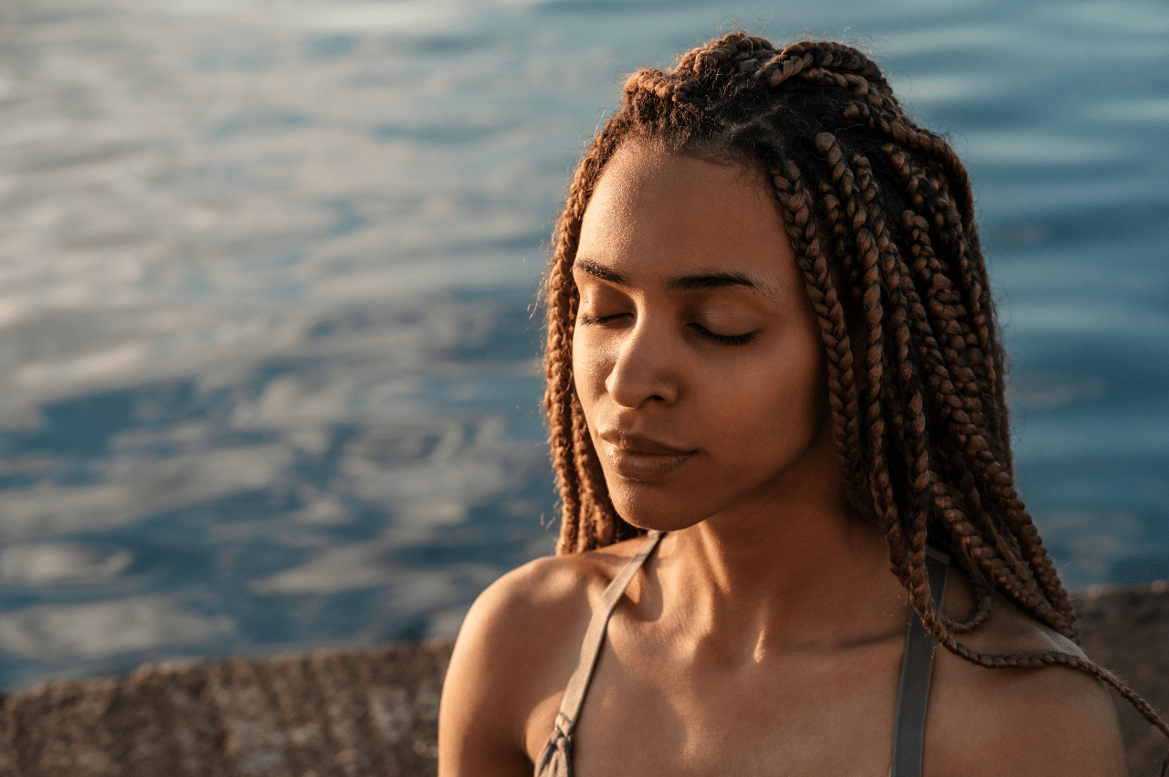 Photo of a woman in front of water with her eyes closed peacefully