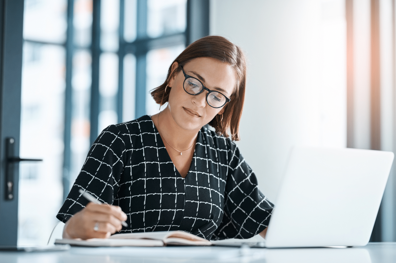 Photo of a woman sitting at a desk with a laptop and notebook open