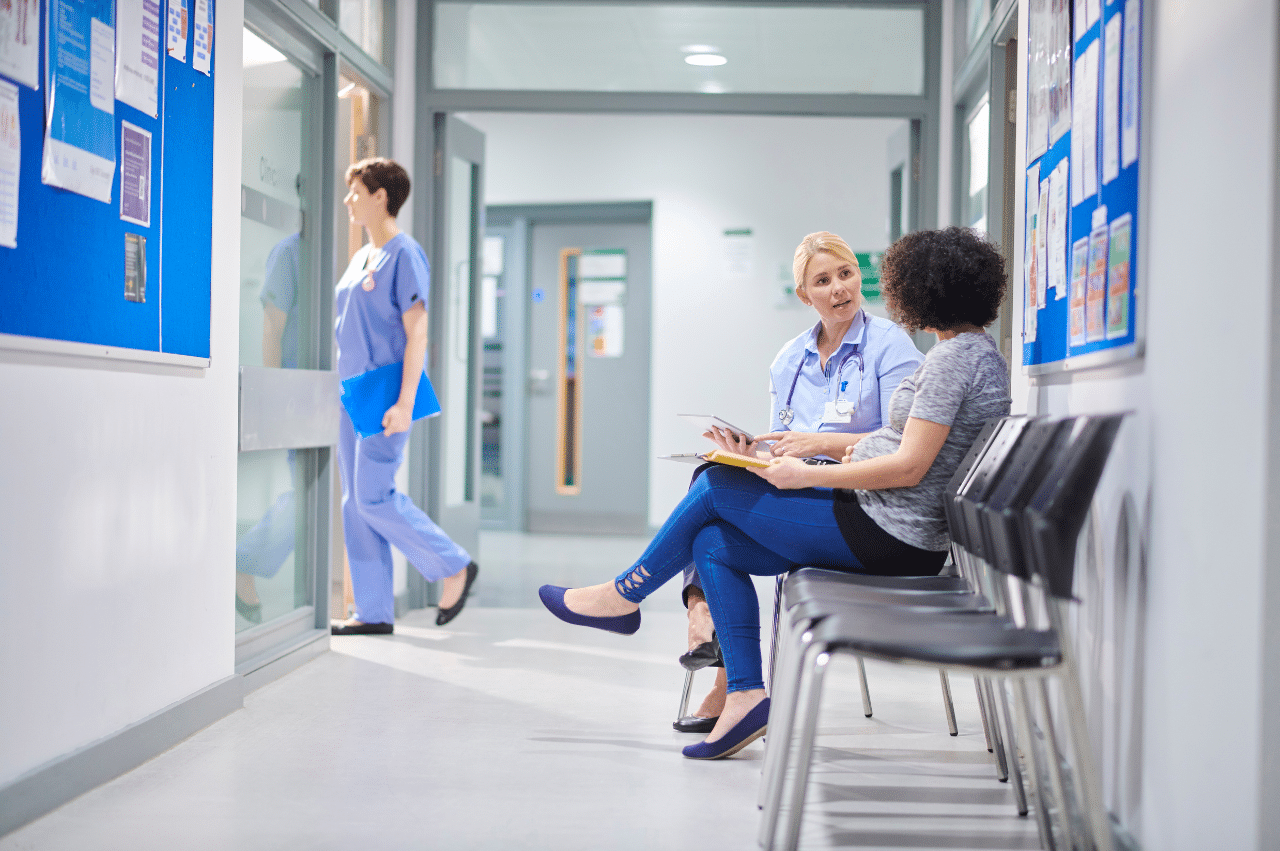 Photo of a clinic hallway. A woman is sitting talking to someone in scrubs