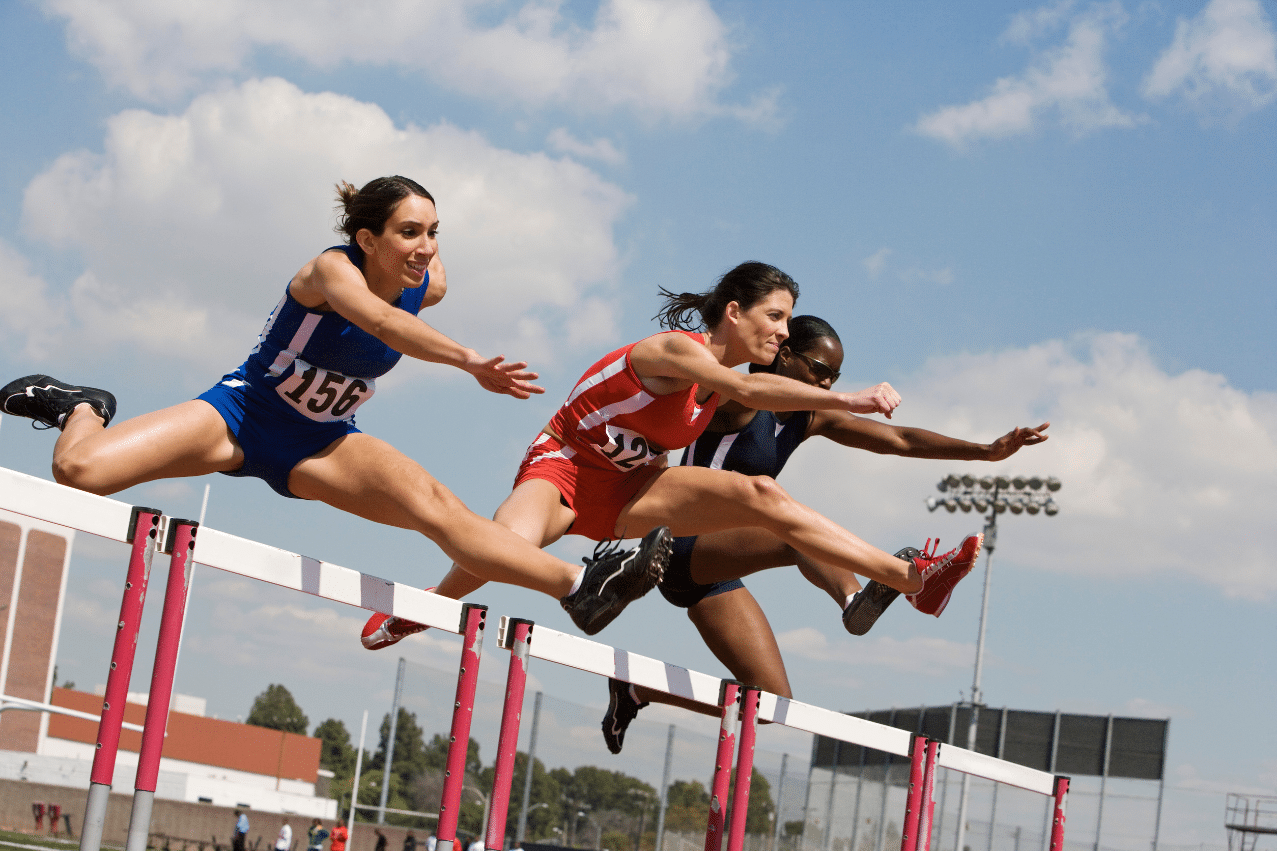 three women track athletes jumping a hurdle