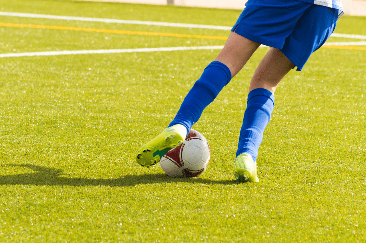 legs kicking soccer ball on field