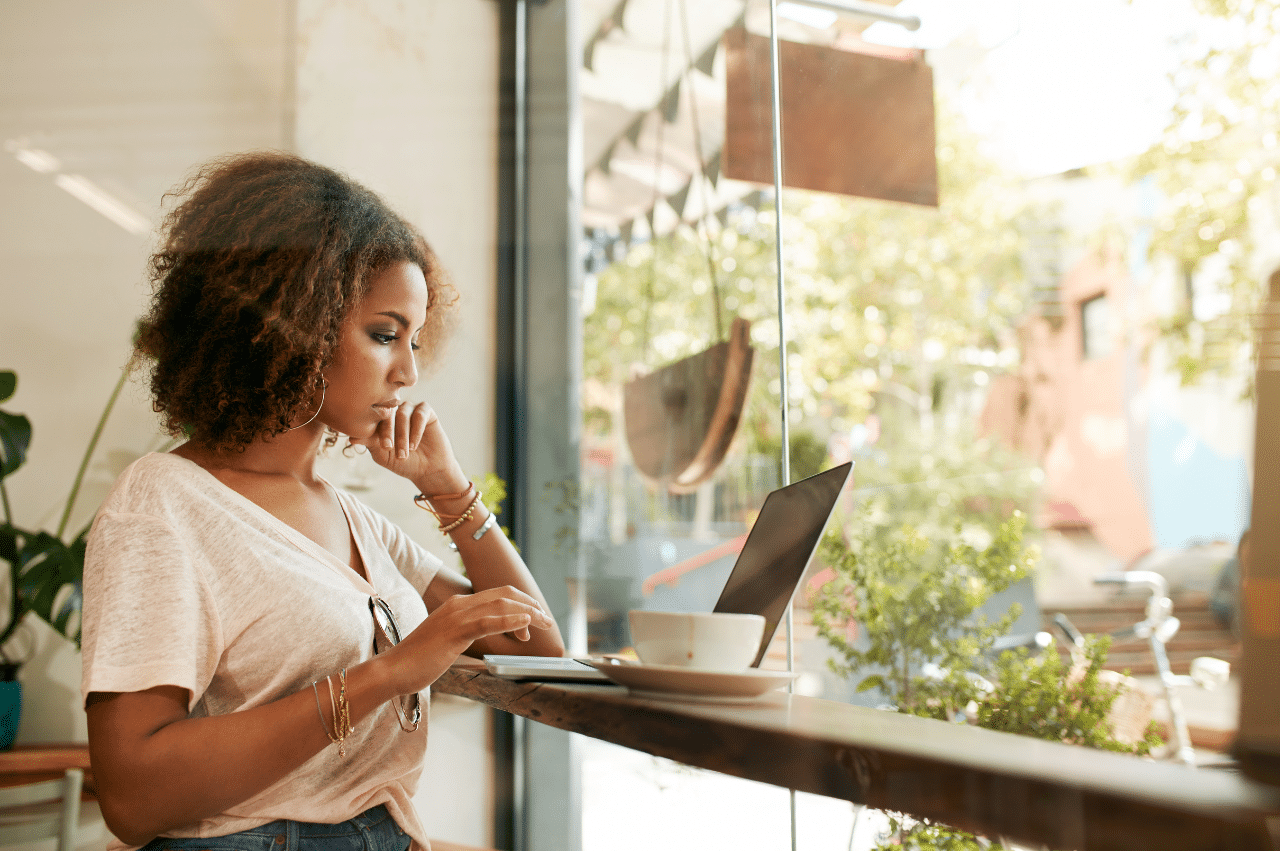 Photo of a Black woman looking at a laptop at a cafe