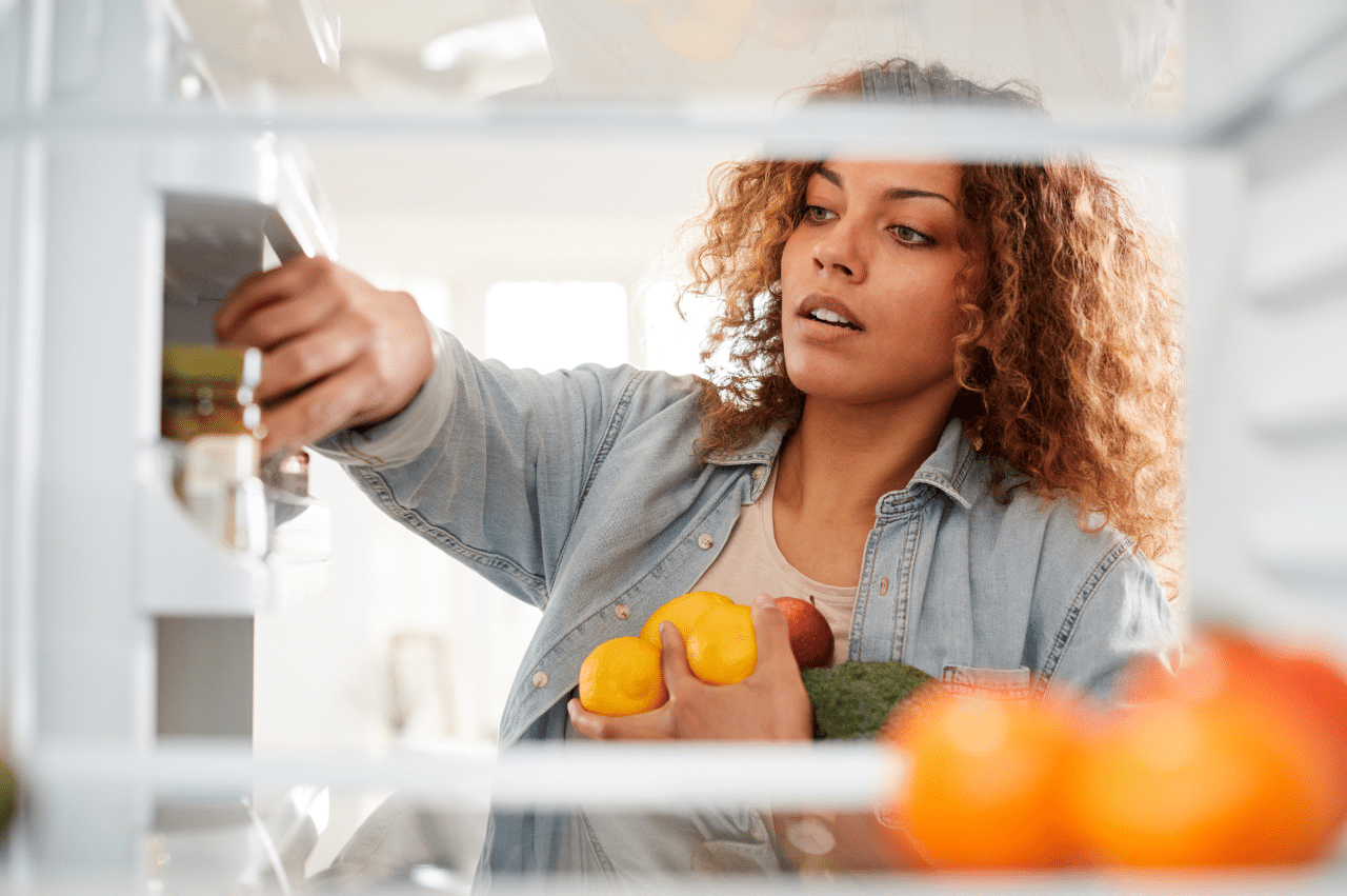 Photo view looking out from inside of refrigerator as woman opens door and packs food onto shelves