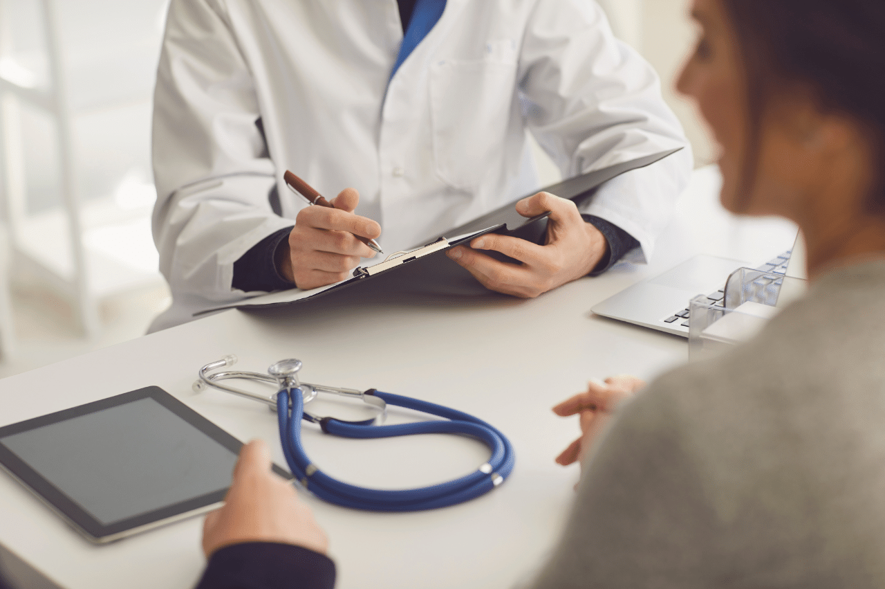 Photo of a doctor writing sitting across a desk from 2 people