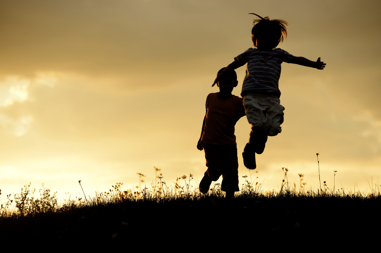 Photo of 2 kids playing in a field at sunset