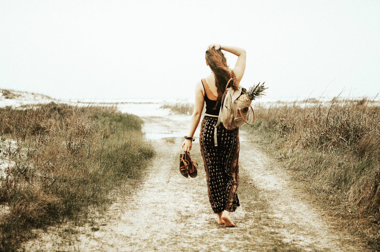 Photo of a woman walking towards a shore through some sandy grass