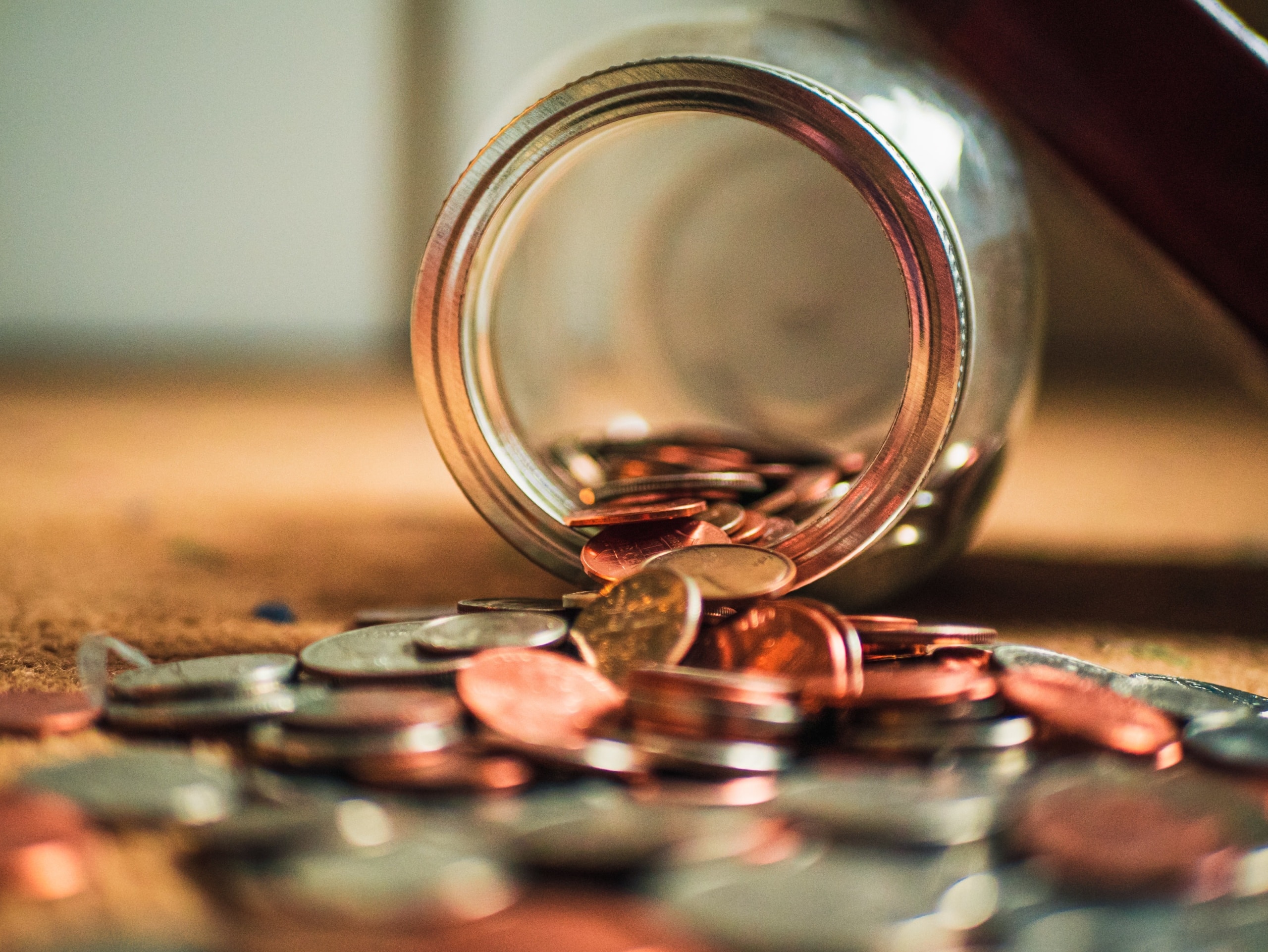 Coins spilling out of mason jar onto table.