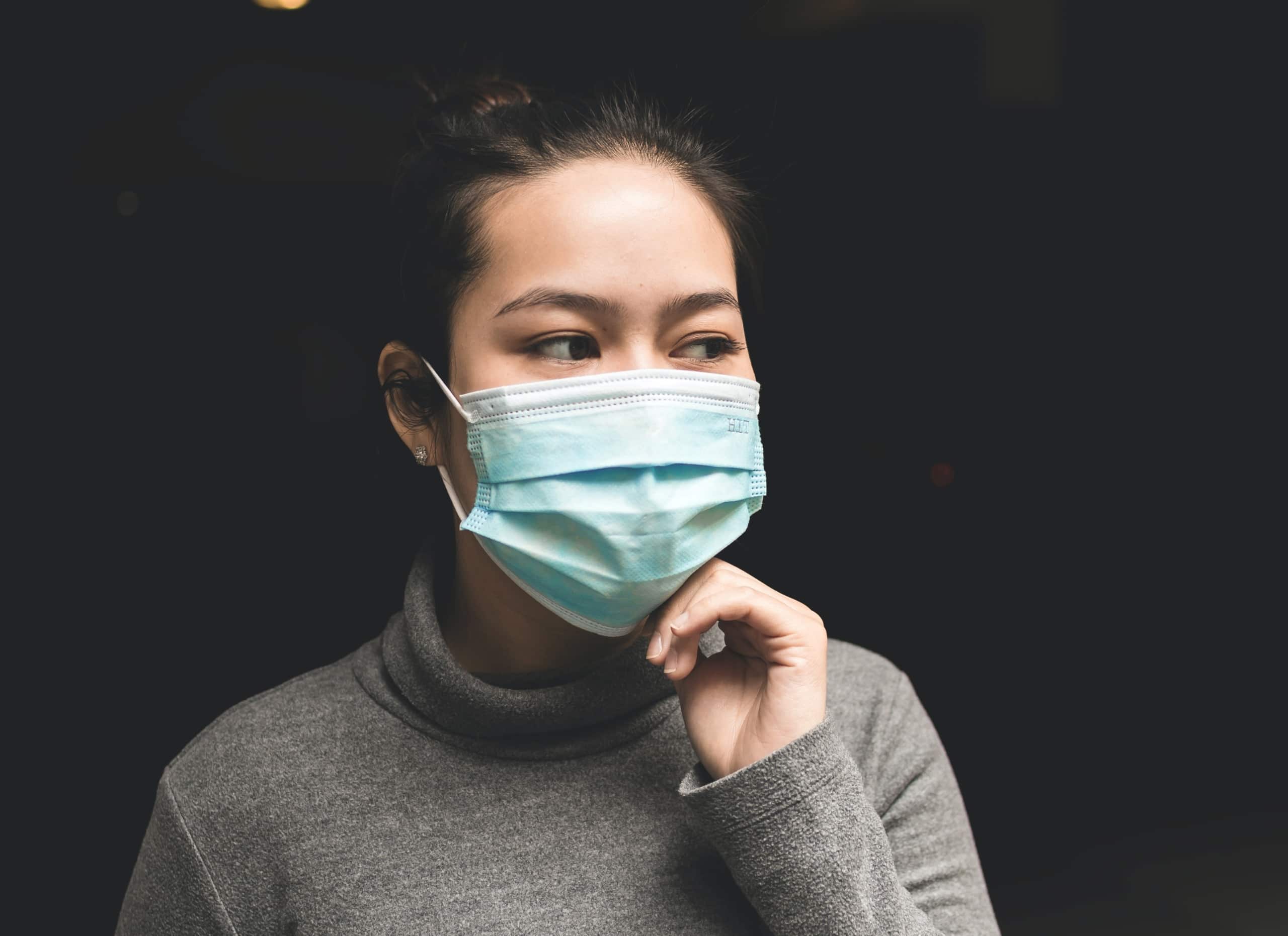 Woman wearing blue mask with black background.