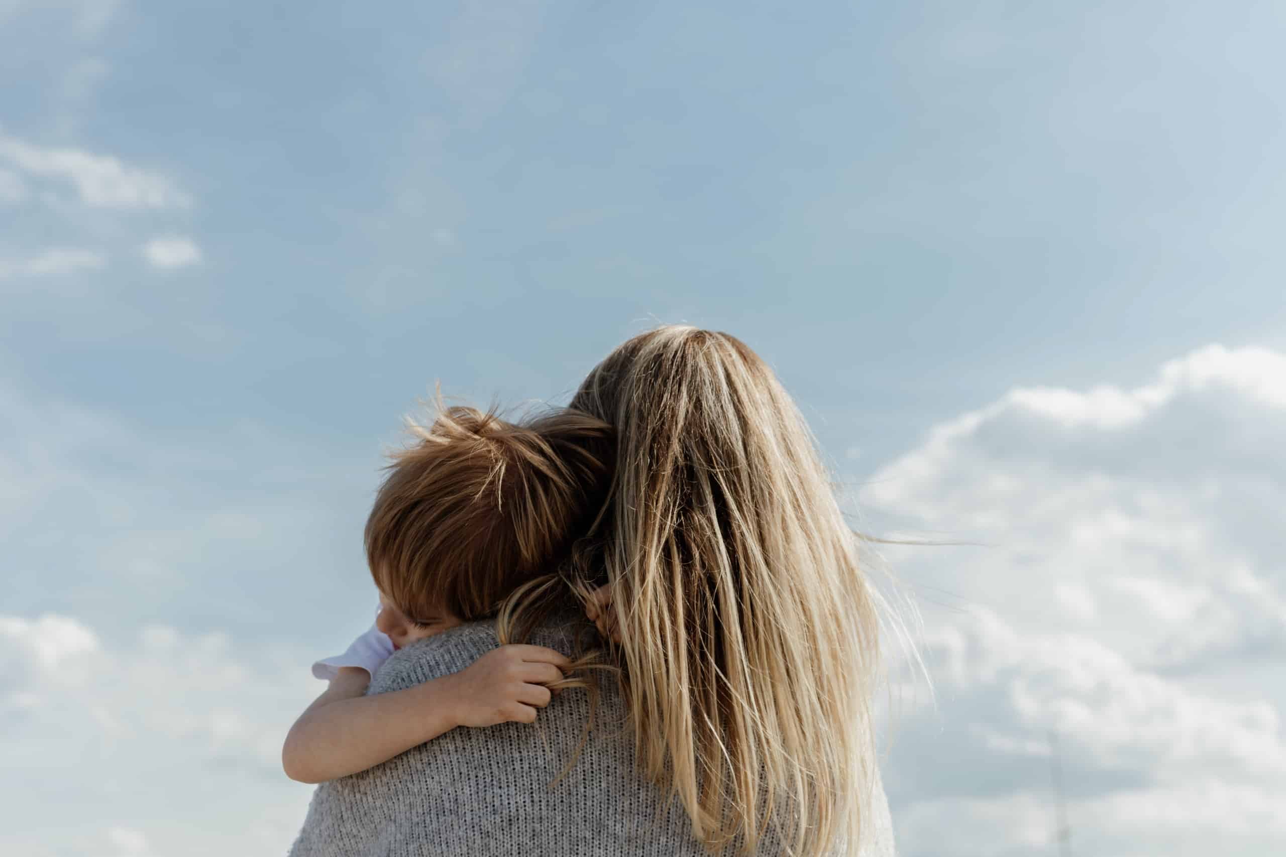 Woman holding child with sky in the background.